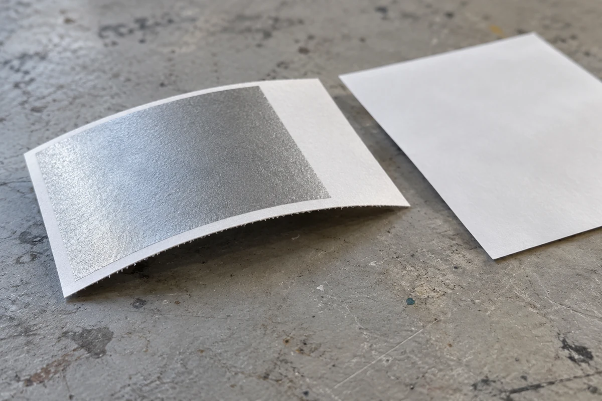 Generated illustration of a bent paper label swatch with a silver patch and visible paper edge